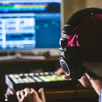 back view of sound engineer in snapback and holding headphones on head monitoring music in studio back view of sound engineer in snapback and holding headphones on head monitoring music in studio