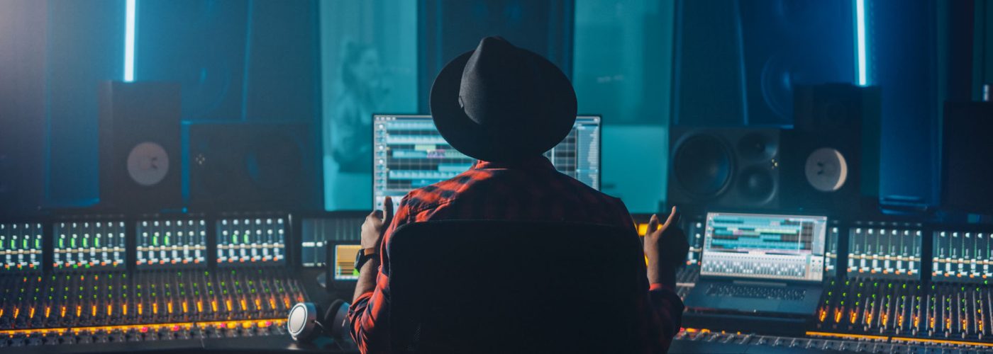 Producer, Audio Engineer Uses Control Desk for Recording New Alb Producer, Audio Engineer Uses Control Desk for Recording New Album Track in Music Record Studio, in the Soundproof Room Musician, Artist, Performer Sings a Song from New Album. Back View